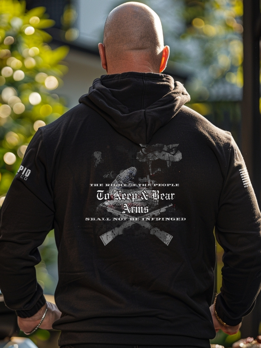 A person wearing a black hoodie with a back 2A design of two crossed rifles, rattlesnakes, and the text "THE RIGHT OF THE PEOPLE TO KEEP AND BEAR ARMS SHALL NOT BE INFRINGED,"