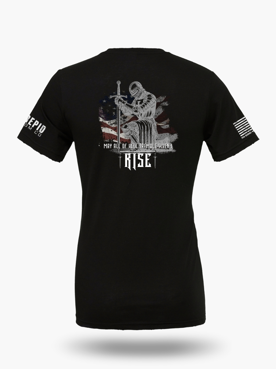 Back view of a black t-shirt with a detailed graphic of a kneeling knight in armor holding a sword, set against an American flag background, and the text "MAY ALL OF HELL TREMBLE WHEN I RISE."