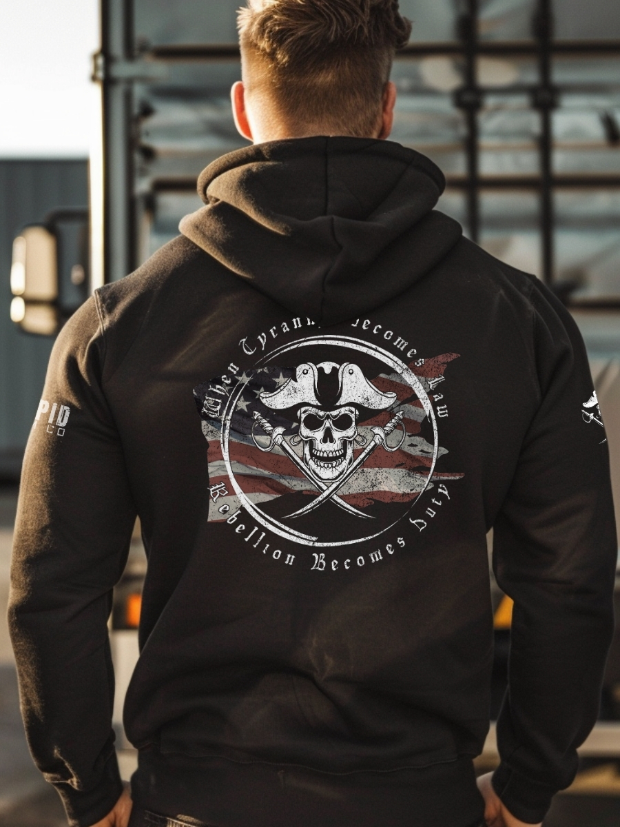 Model wearing black patriotic hoodie inspired by Revolutionary privateers, featuring pirate skull, swords, and anti-tyranny text over a worn U.S. flag.